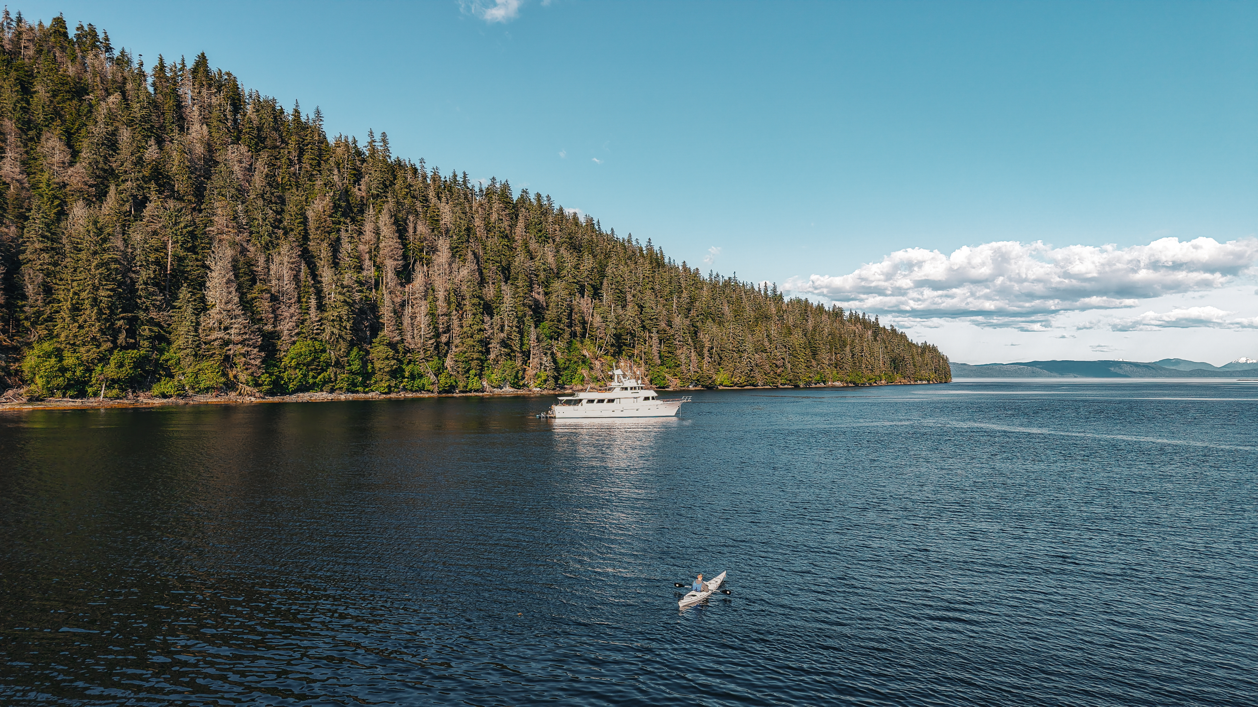 Motor Yacht Oceana anchored in a sheltered Southeast Alaska cove with a kayaker nearby